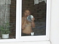 A hot topless chick puts on her makeup by a window